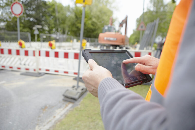 man wearing vest holding iPad next to road construction